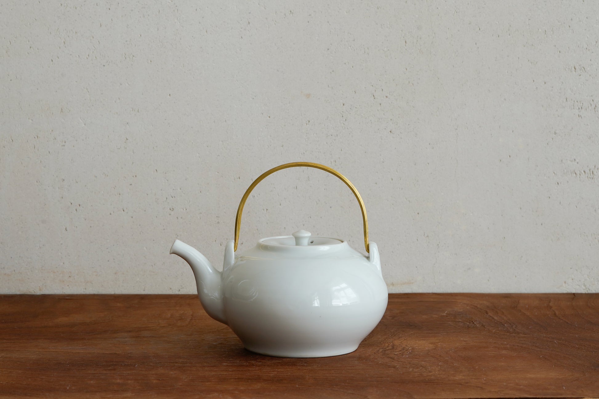 White ceramic teapot with a gold handle on a wooden surface and beige background